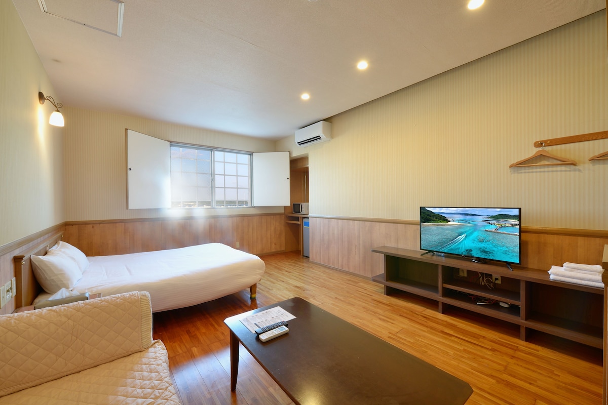 A hotel room with a bed, a sofa, a TV, and a wooden floor.