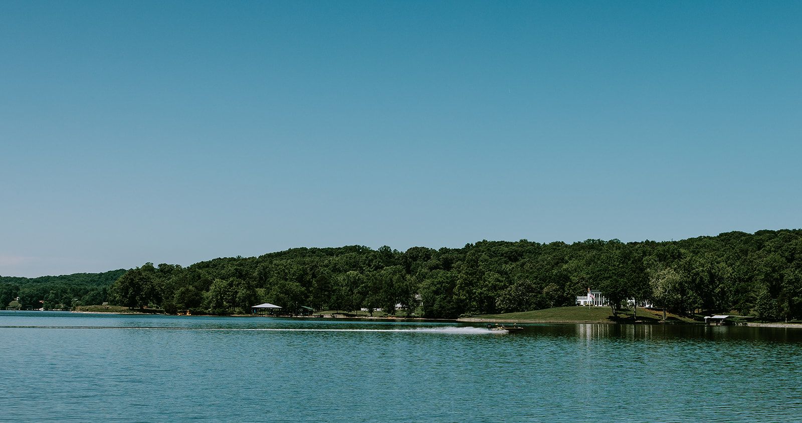 A lake with a dock, a gazebo, and a building on a hill.