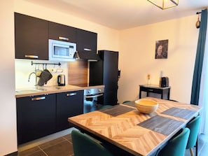 A modern kitchen with dark cabinetry, a microwave, and a built-in oven. There is a dining table with a wooden herringbone pattern table runner and a large wooden bowl. - L'Alpin (4 People) Balcony with a view of the mountains—close to the train station and the gondola. Indoor parking. (Saint-Gervais-les-Bains)