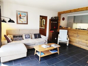 A living room with a sofa, a coffee table, and a kitchen area with cabinets and a sink. - The Onyx (2 people) View of Mont Blanc and close to the slopes. (Saint-Gervais-les-Bains)