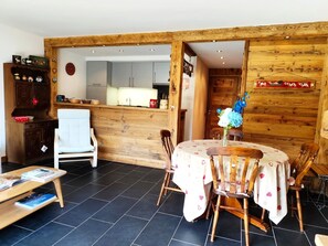 A dining area with a round table, chairs, a wooden cabinet, and a kitchen in the background. - The Onyx (2 people) View of Mont Blanc and close to the slopes. (Saint-Gervais-les-Bains)