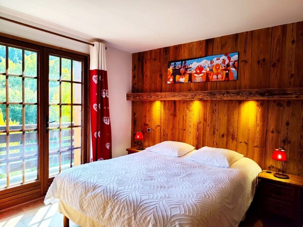 Een slaapkamer met een groot bed, een houten hoofdbord, twee nachtkastjes met lampen en een raam met gordijnen.