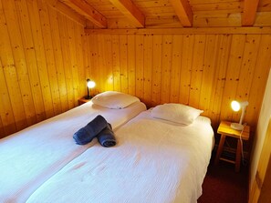 Ein Einzelbett mit weißer Bettwäsche, zwei Kissen und einem zusammengerollten Handtuch in einem Raum mit Holzwänden und einer geneigten Decke.