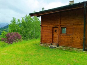 Eine hölzerne Hütte mit Tür und Fenster, umgeben von Gras und Bäumen.