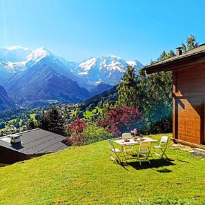 Blick auf Berge mit einem Holzhaus und einer Essecke inklusive Tisch und Stühlen.