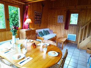 Ein Interieur einer Holzhütte mit einem für das Frühstück gedeckten Esstisch, einer Couch und einer Treppe.