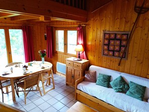 A cozy cabin interior with a dining table, chairs, a sofa, and a lamp. - Le Mazot (sleeps 5) Mountain view, close to the slopes. Indoor parking. (Saint-Gervais-les-Bains)