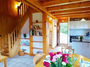 Een houten interieur met een trap, een eethoek met een tafel en stoelen, en een keuken met kastjes en een spoelbak.