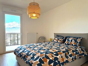 A bedroom with a large bed, a hanging light fixture, a window with a view, and a radiator. - La Belle Vue (4 people) Terrace with a view of the mountains. Indoor parking (Saint-Gervais-les-Bains)