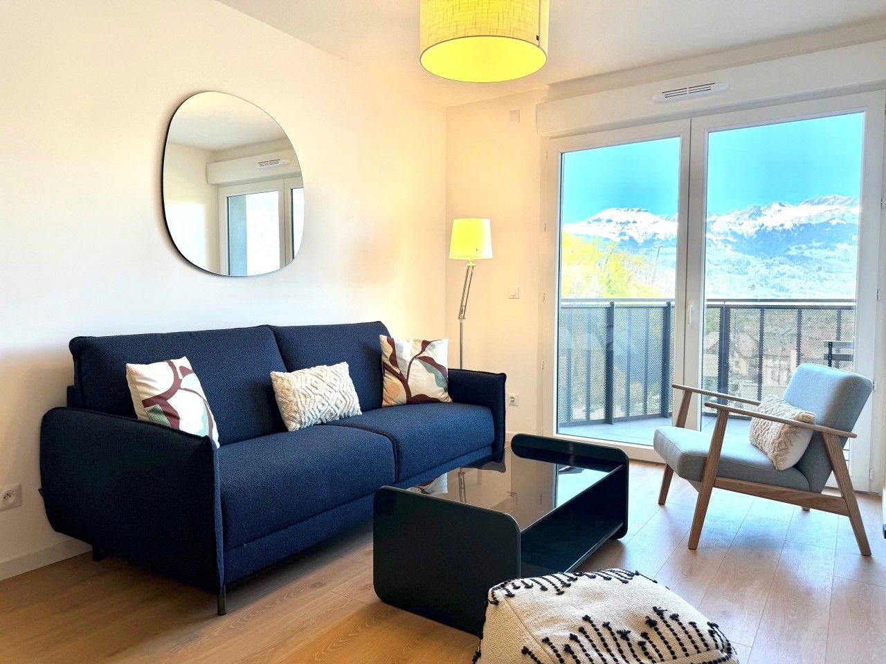 Un salon moderne avec un canapé, une table basse et un fauteuil. Une grande fenêtre offre une vue sur les montagnes.