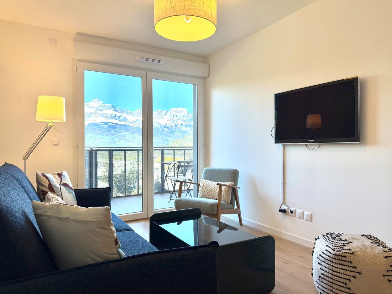 Un salon moderne avec un canapé, un fauteuil et un téléviseur fixé au mur.