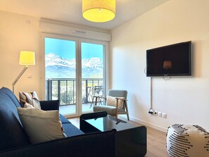 A modern living room with a sofa, armchair, and a television mounted on the wall. - La Belle Vue (4 people) Terrace with a view of the mountains. Indoor parking (Saint-Gervais-les-Bains)