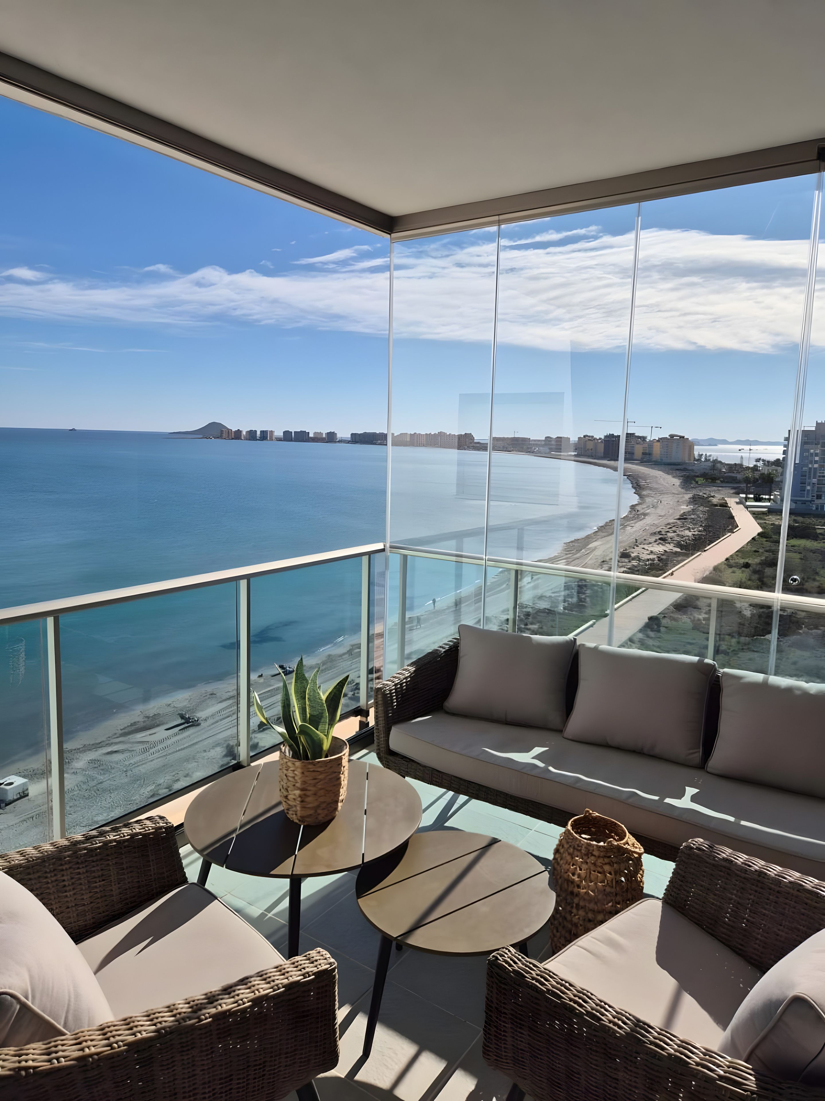 Un balcon avec vue sur la plage et l’océan, aménagé avec des fauteuils et une table en osier.