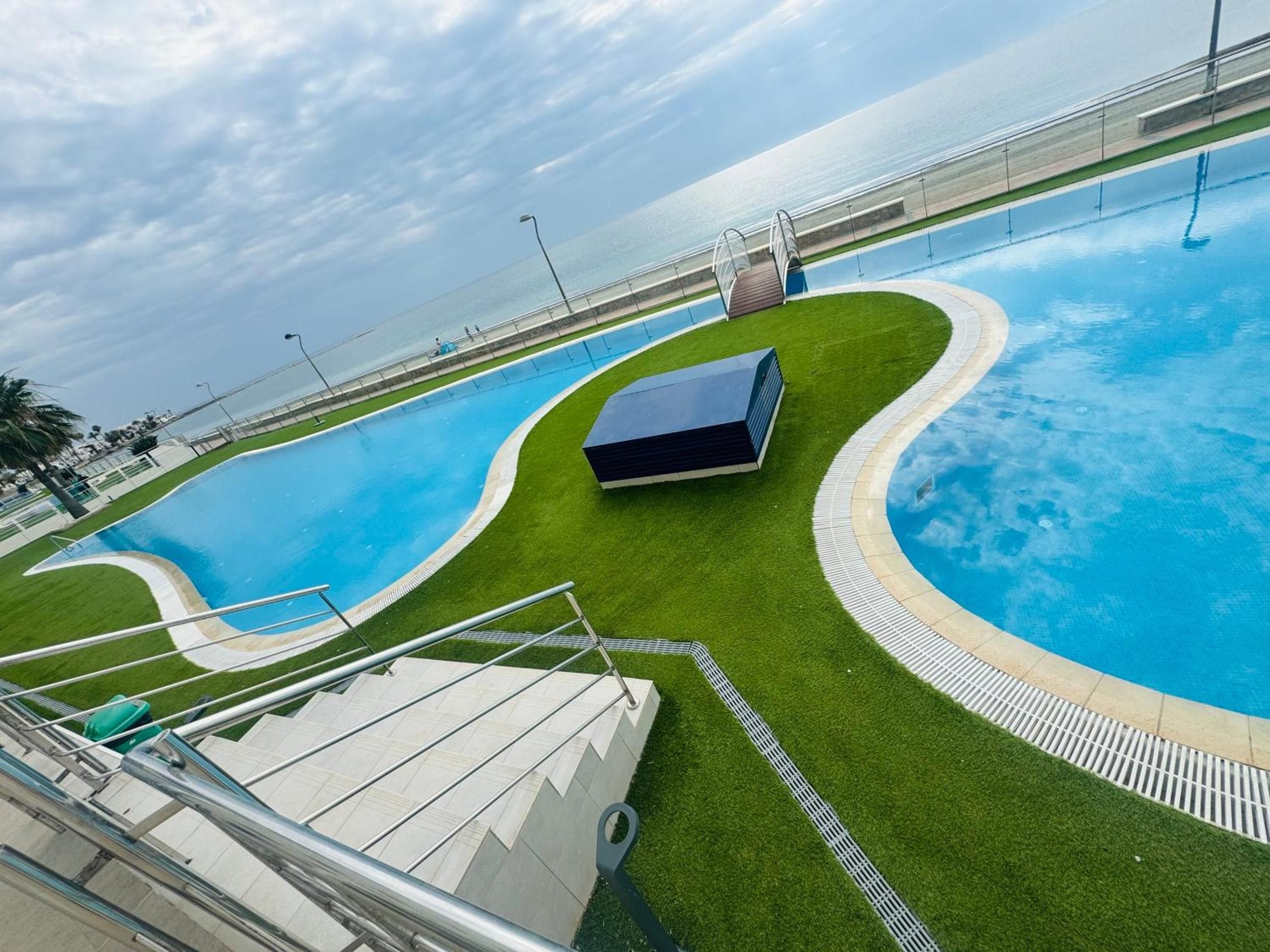 A swimming pool with a curved design, surrounded by artificial grass and a small building structure.