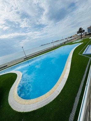 En swimmingpool med en buet kant, omgivet af grøn kunstgræs og en belagt sti.