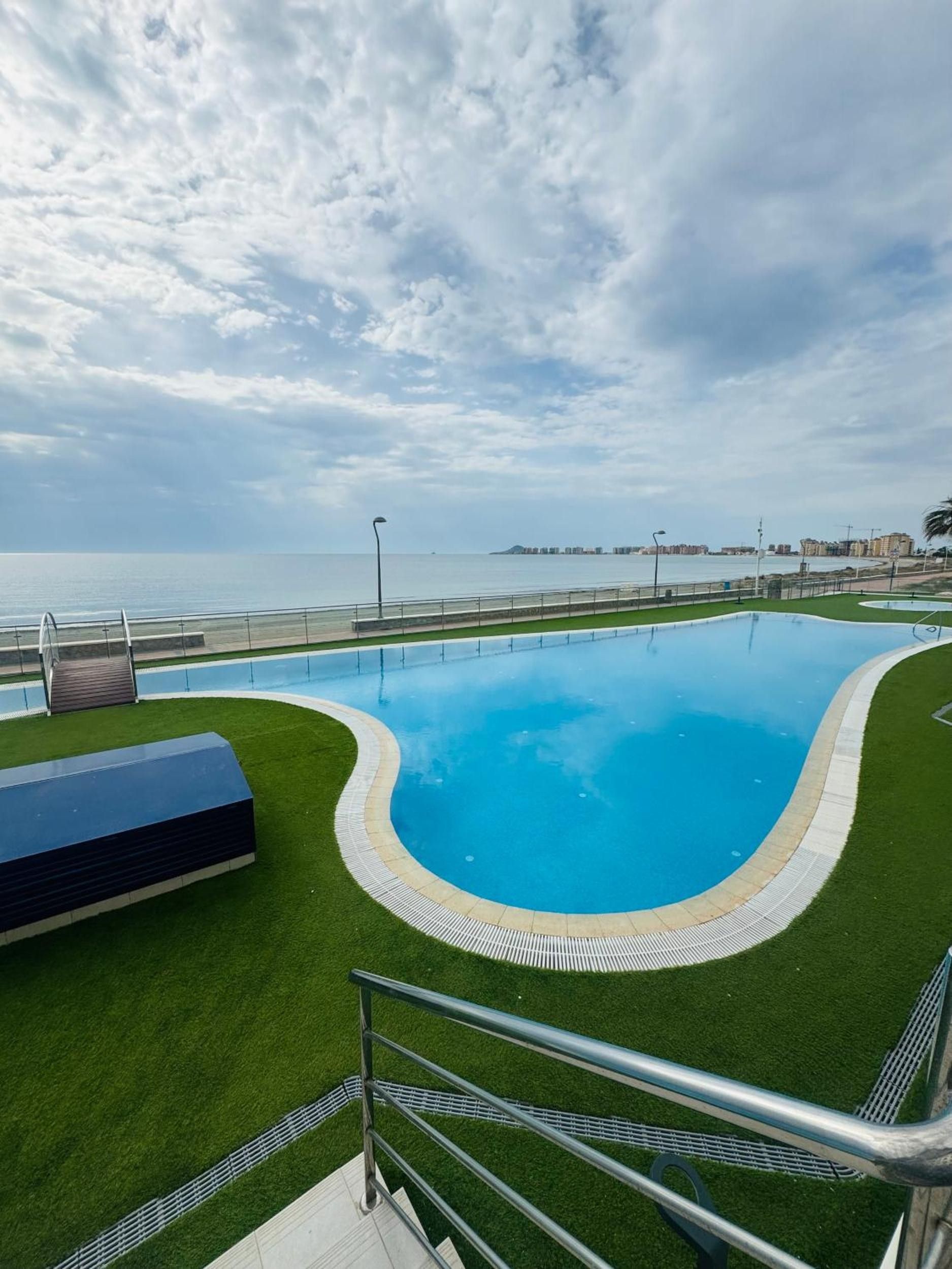 Une piscine avec vue sur la mer, entourée de pelouse et bordée d’une rambarde en métal.
