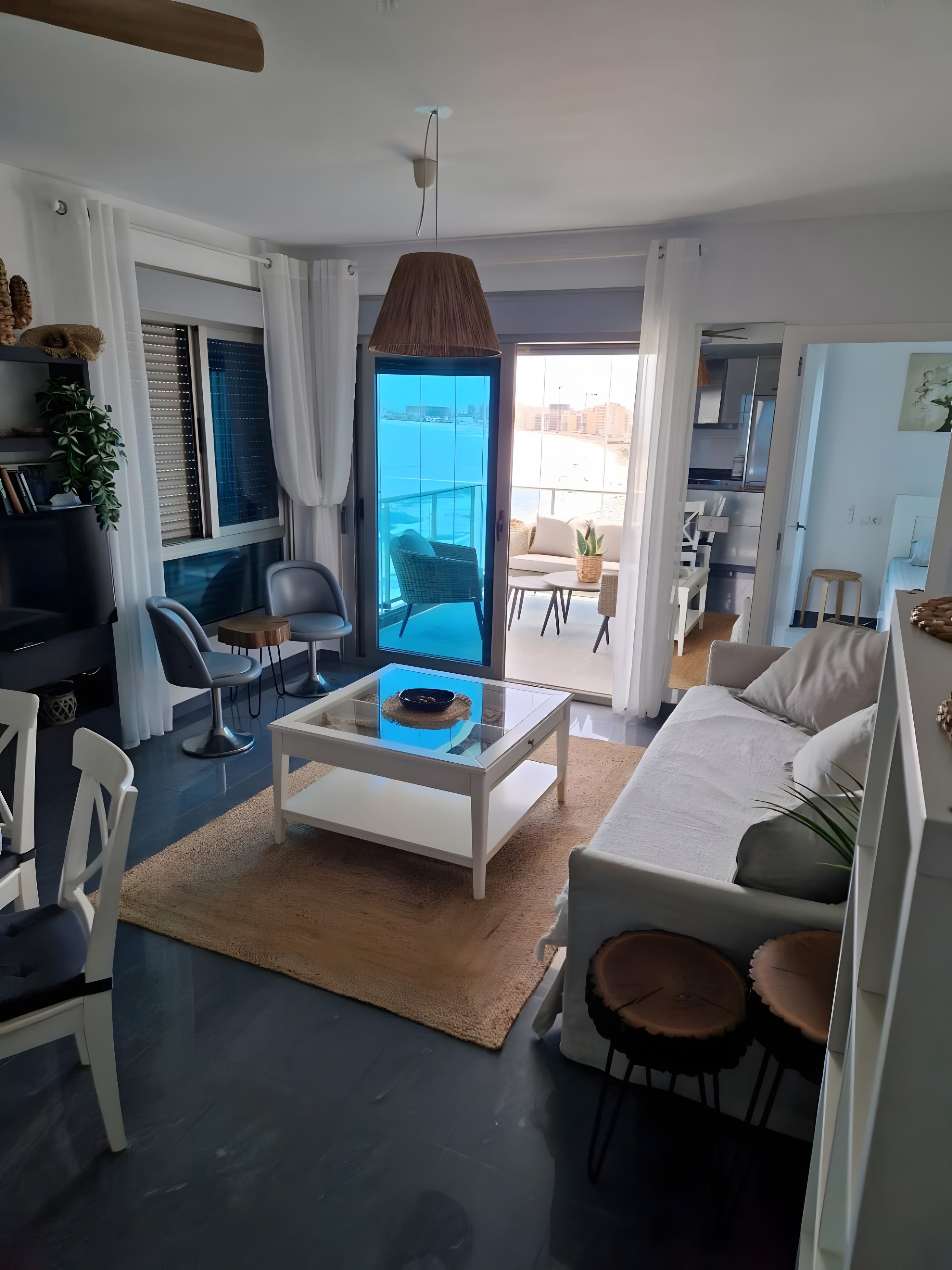Una sala de estar moderna con una mesa de centro de vidrio, zona de estar y vista al mar.