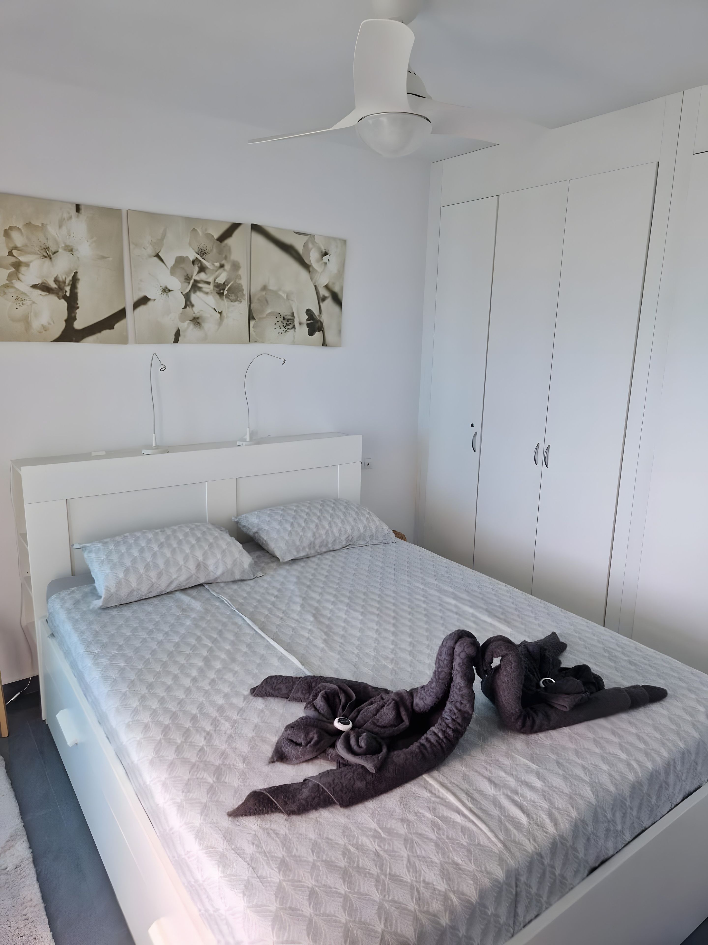 Une chambre à coucher comprenant un lit, un ventilateur de plafond, une lampe fixée au mur et une armoire.