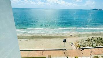 Blick auf einen Strand mit Poolbereich, klarem Himmel und dem Meer.