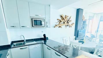A modern kitchen with white cabinetry, a built-in microwave, and a wooden cutting board on the countertop.