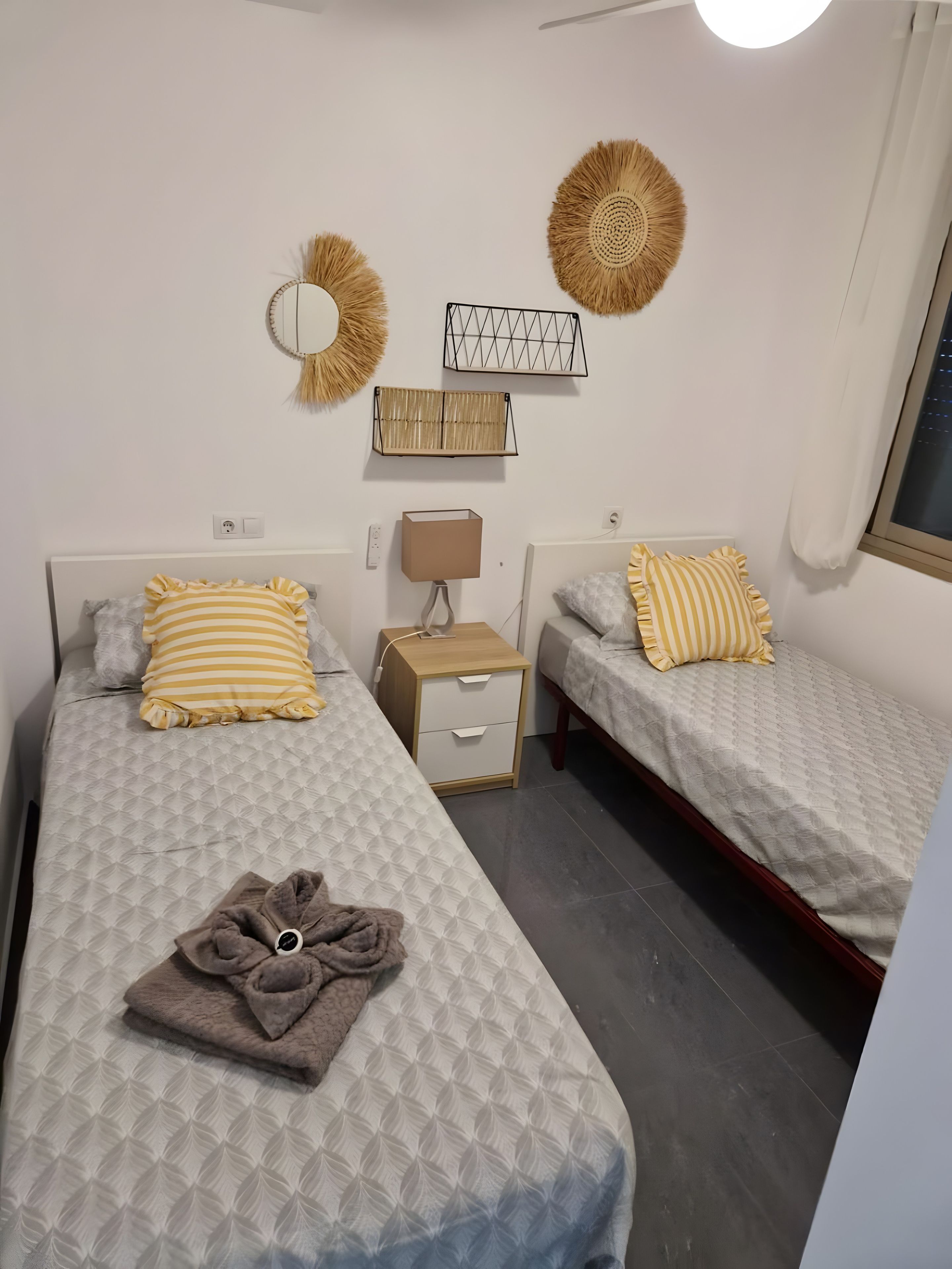 Quarto com duas camas, mesa de cabeceira, abajur e decoração na parede.