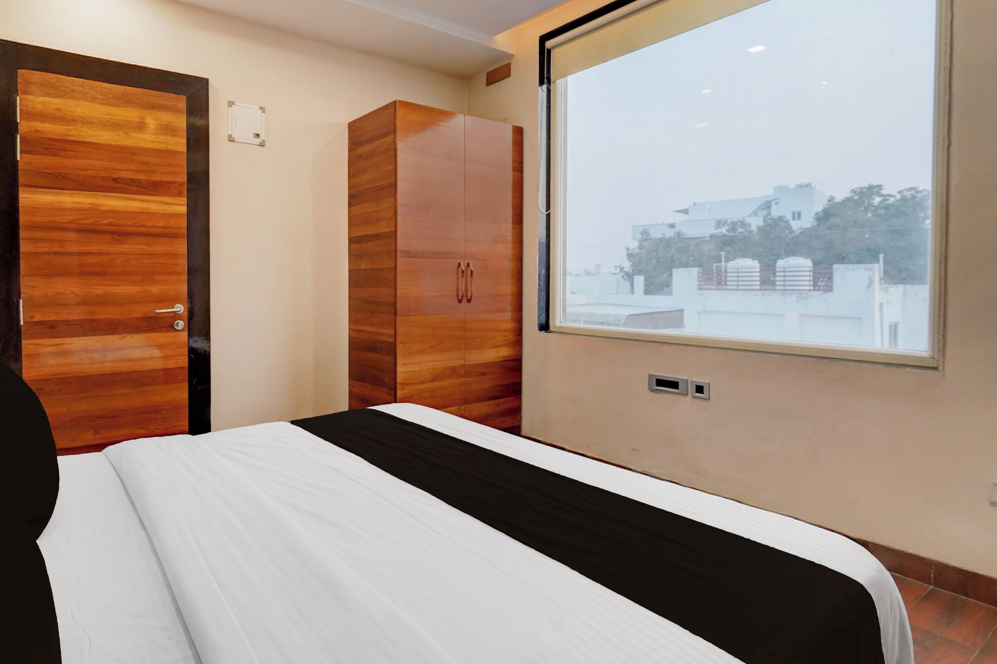 A bedroom with a bed, wardrobe, and a window with a view of buildings.
