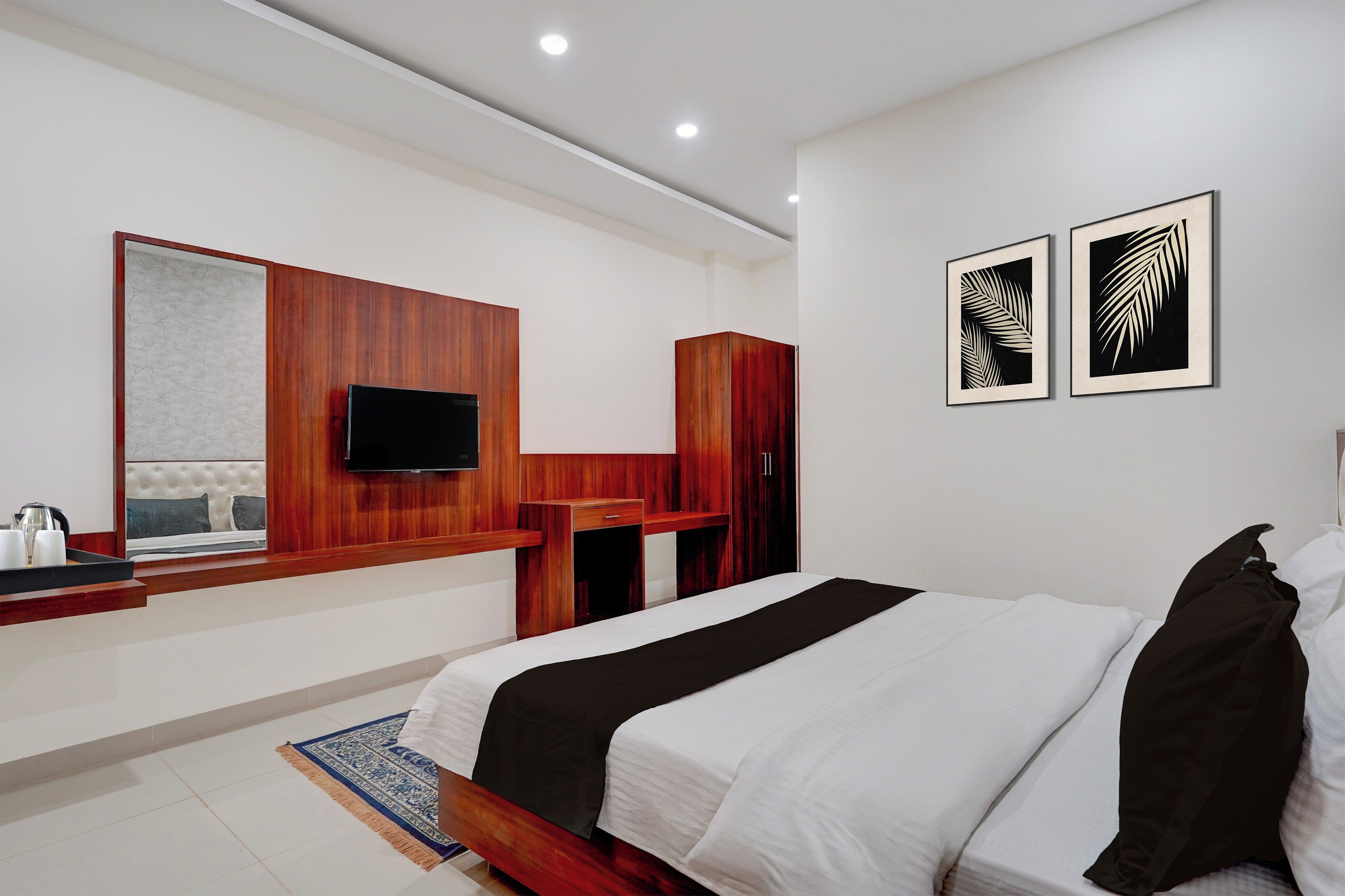 Habitación de hotel con cama, televisor montado en un panel de madera, un pequeño escritorio y dos obras de arte enmarcadas en la pared.