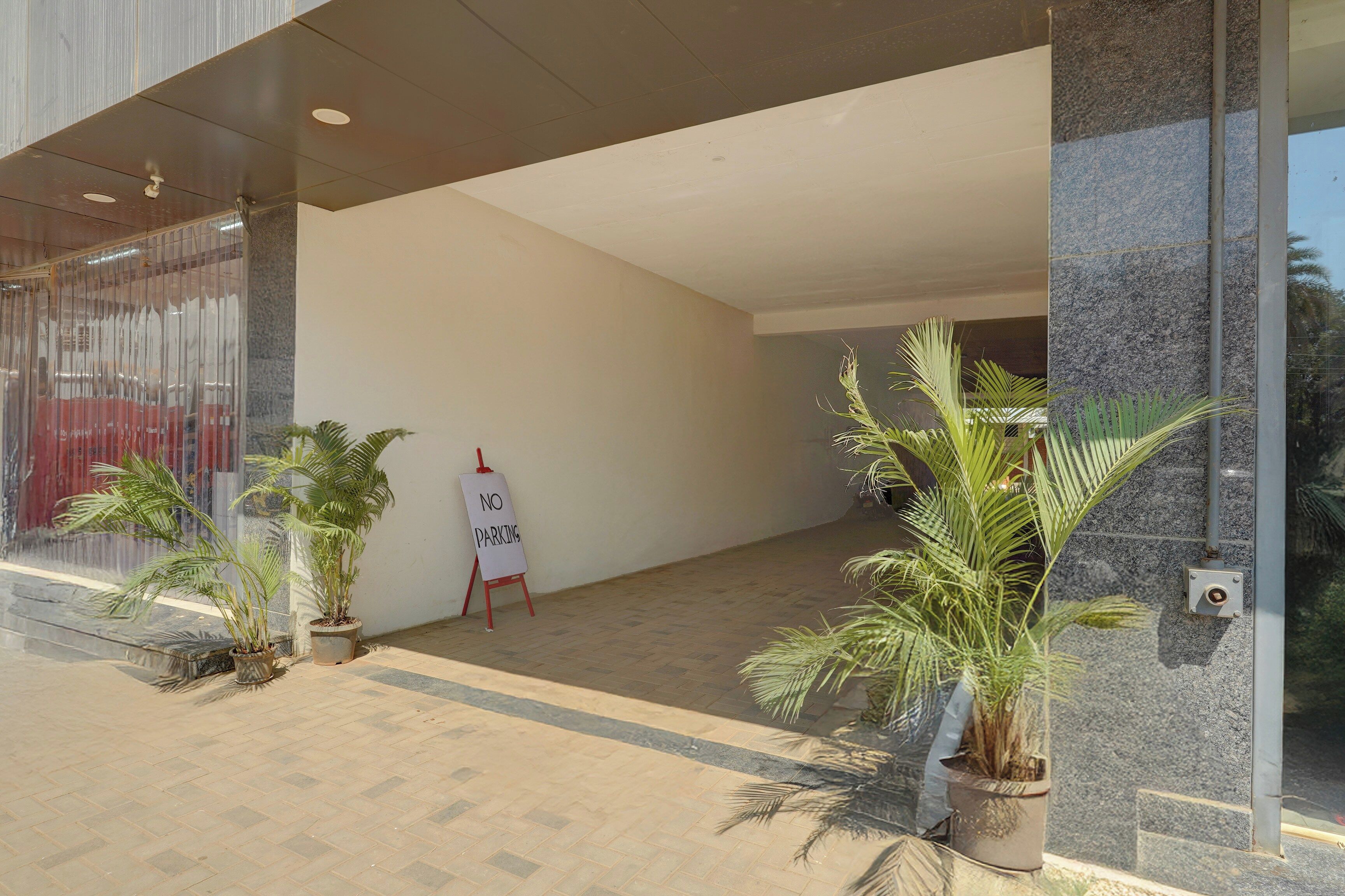 A building entrance with a 'NO PARKING' sign, potted plants, and a tiled floor.