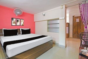 A hotel room with a bed, a wall-mounted fan, a door with a sign, and a window with curtains.