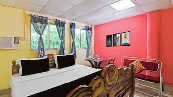 Una habitació d'hotel amb llit, taula, cadires i obres d'art a les parets.