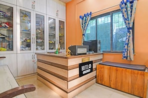 Una taulell de recepció amb un rètol que diu 'HOTEL & Company Serviced', una finestra amb cortines estampades i un moble amb portes de vidre que conté diversos objectes.