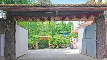 Una entrada protegida por un portón, con una estructura decorativa y un camino de concreto que lleva a un edificio.