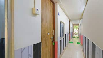 Passadís amb portes d'un costat i finestres de l'altre, que condueix a una habitació amb vista a la vegetació.