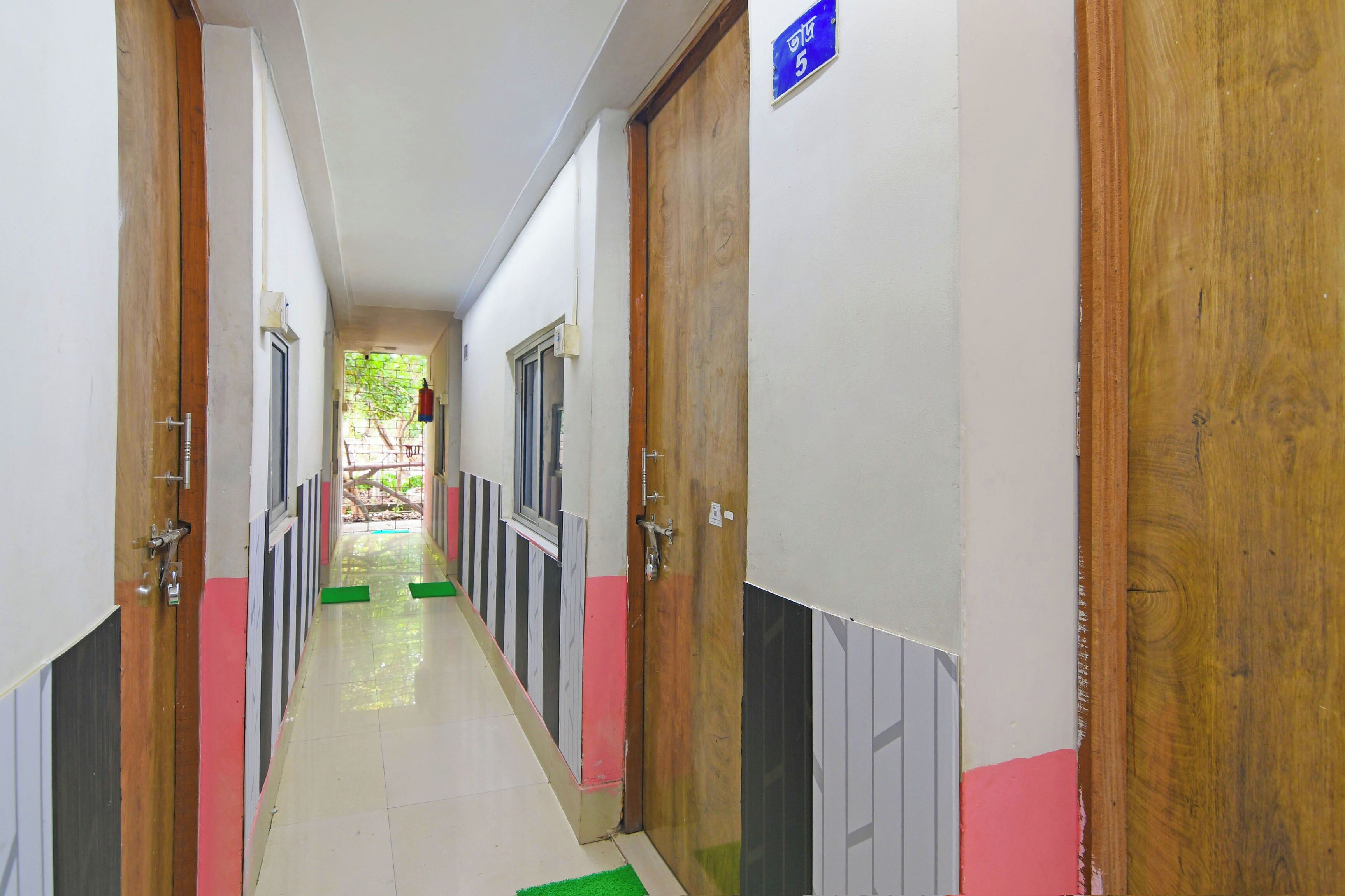 Un pasillo con puertas a ambos lados, suelo de baldosas y un letrero azul que indica la habitación número 5.