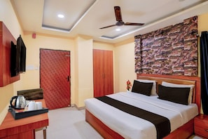 A hotel room with a bed, bedside tables, a ceiling fan, a wall-mounted TV, and a patterned tapestry. - Super OYO Collection O BHU Road Varanasi (Varanasi)