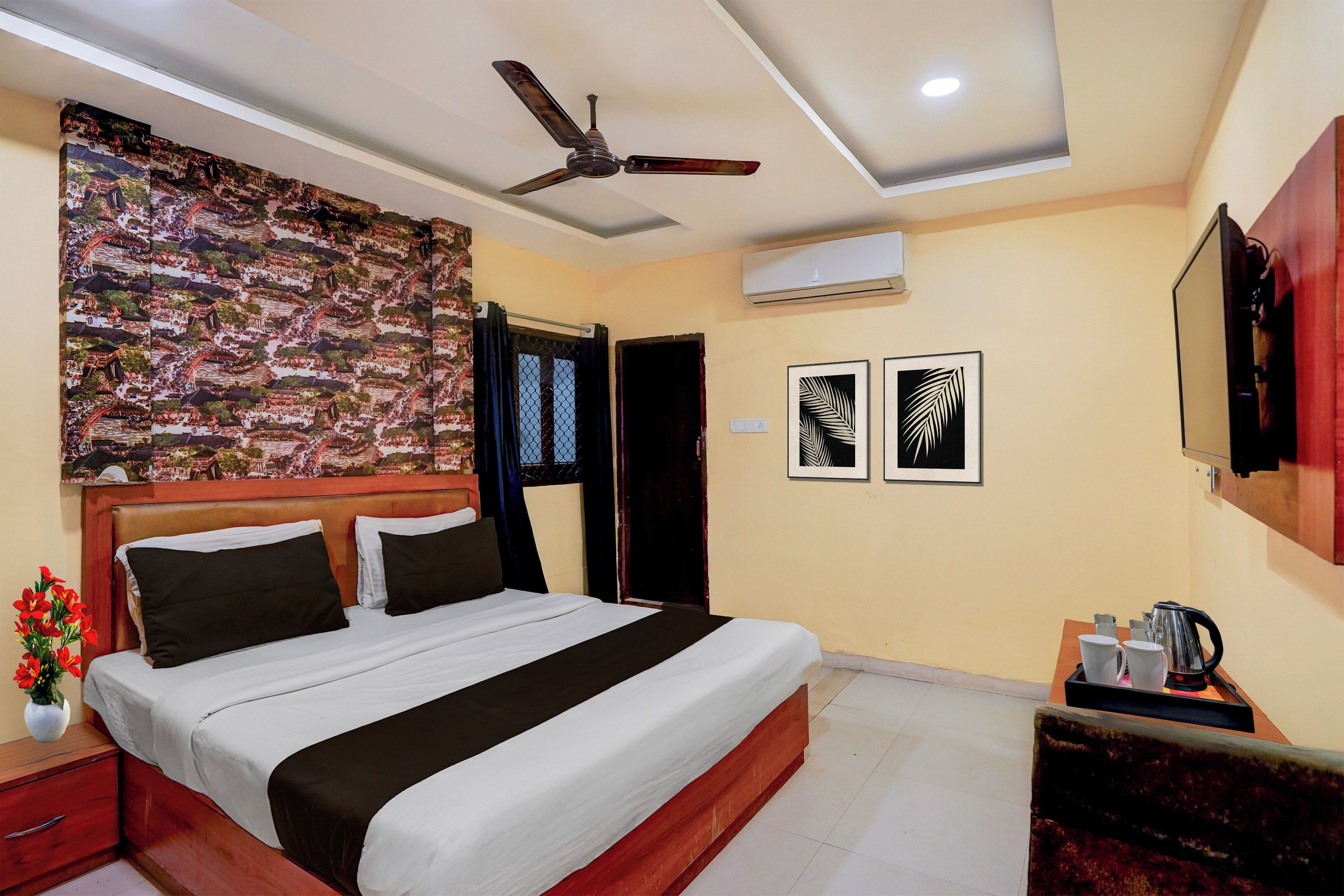 Une chambre d’hôtel équipée d’un lit, d’un ventilateur de plafond, d’un climatiseur, d’une table de chevet, d’une machine à café et d’un tableau encadré au mur.