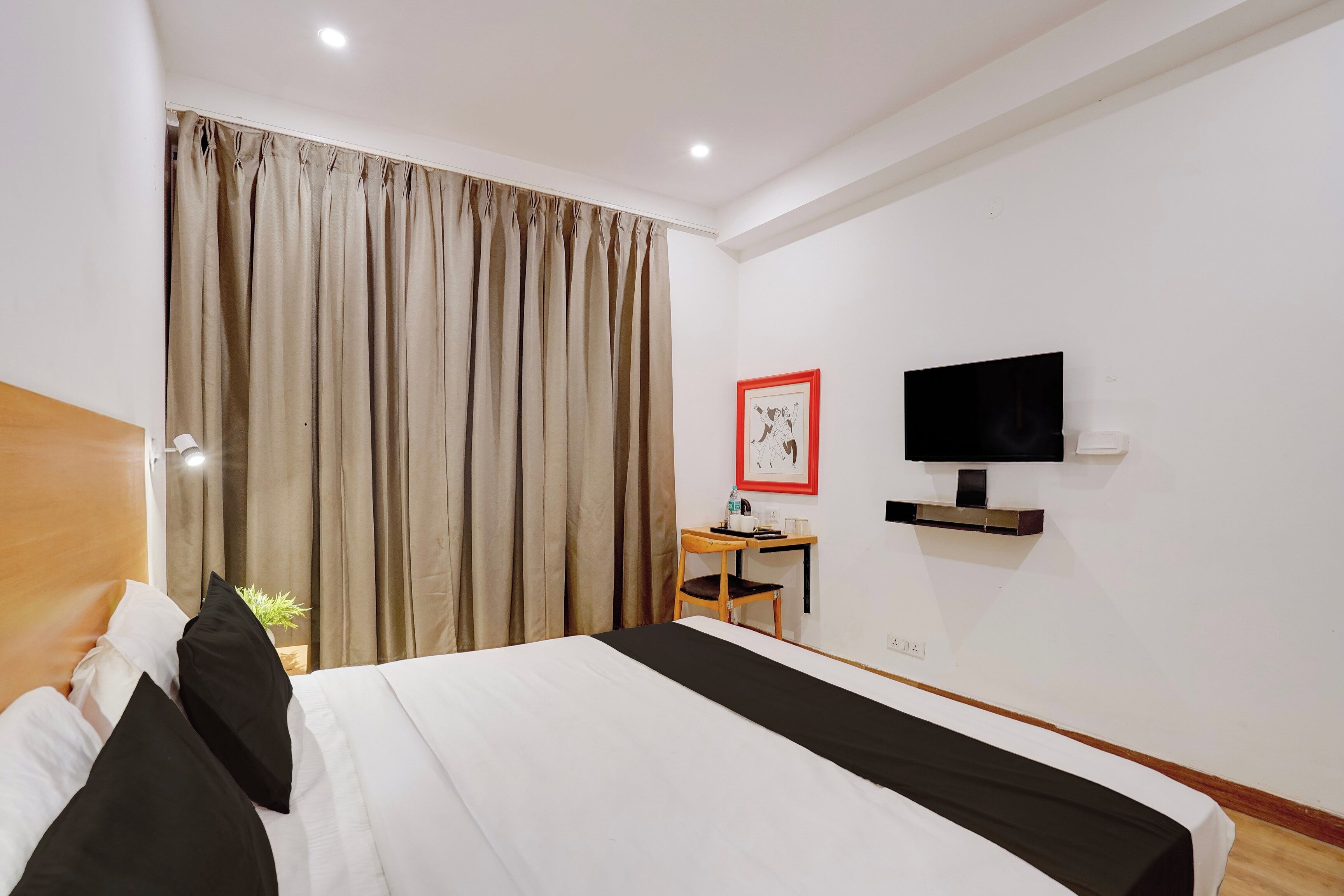 Habitación de hotel con cama, escritorio con silla, televisor y un cuadro en la pared.