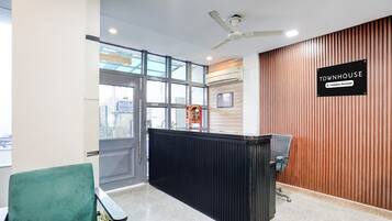 Un área de recepción con un mostrador negro, una silla verde y un ventilador de techo.