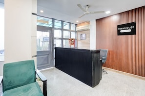 A reception area with a black reception desk, a green chair, and a ceiling fan. - Townhouse Sector 39 Gurgaon (Gurugram)