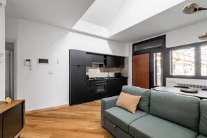 Una cucina moderna con mobili neri, forno integrato e zona pranzo con divano grigio e tavolo in legno.
