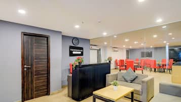 Una zona de recepción con un reloj, un cartel que indica servicio de la empresa y un área de descanso con sillas rojas.