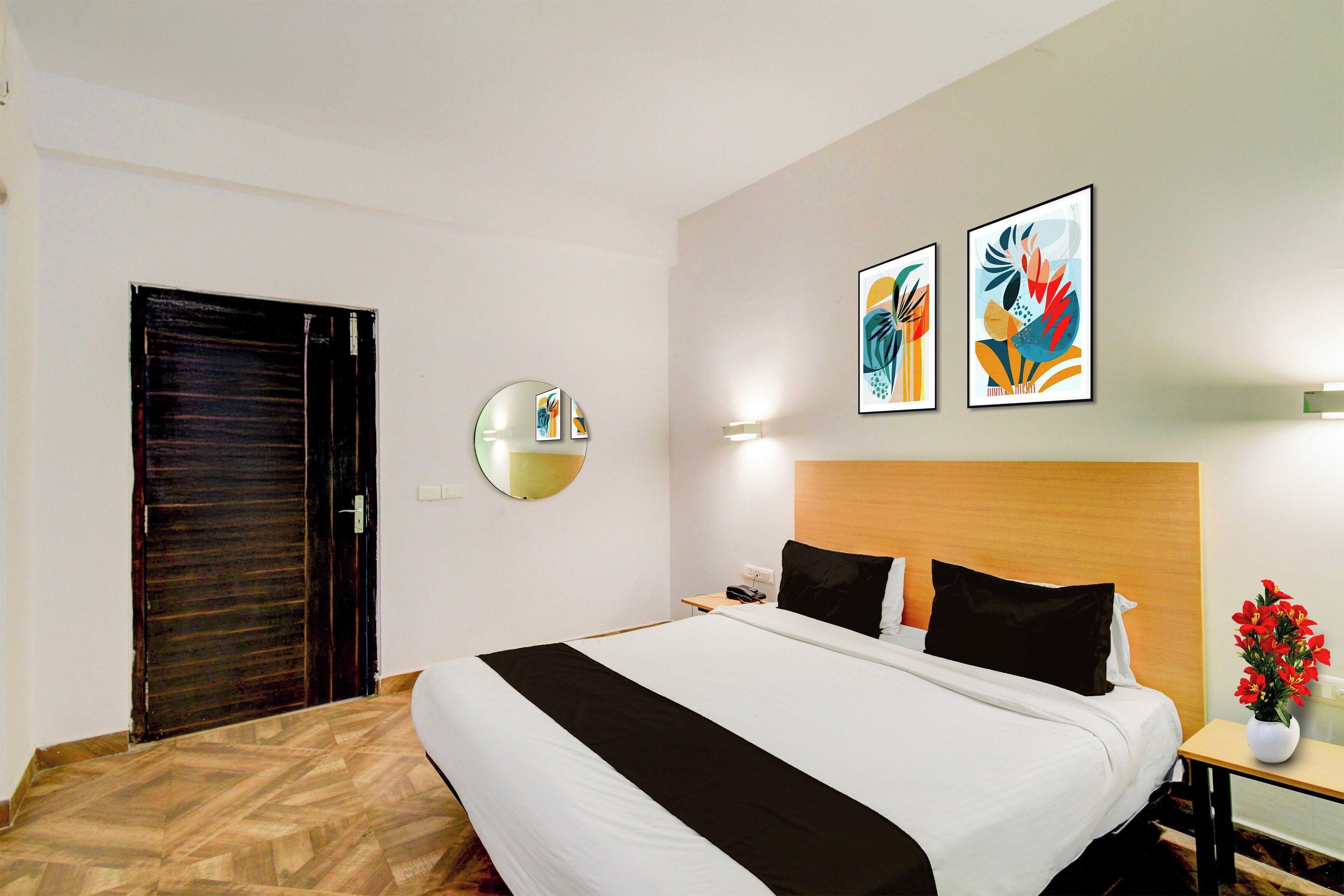 Ein Hotelzimmer mit einem Bett, einem Nachttisch mit einer Vase und zwei an der Wand befestigten Kunstwerken.