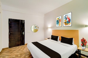 Una habitación de hotel con una cama, una mesita de noche con un florero y dos obras de arte colgadas en la pared.