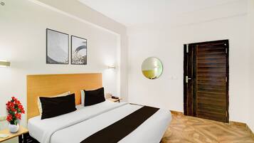 Una habitación de hotel con una cama, una mesita de noche con un jarrón de flores, un espejo redondo y una puerta.