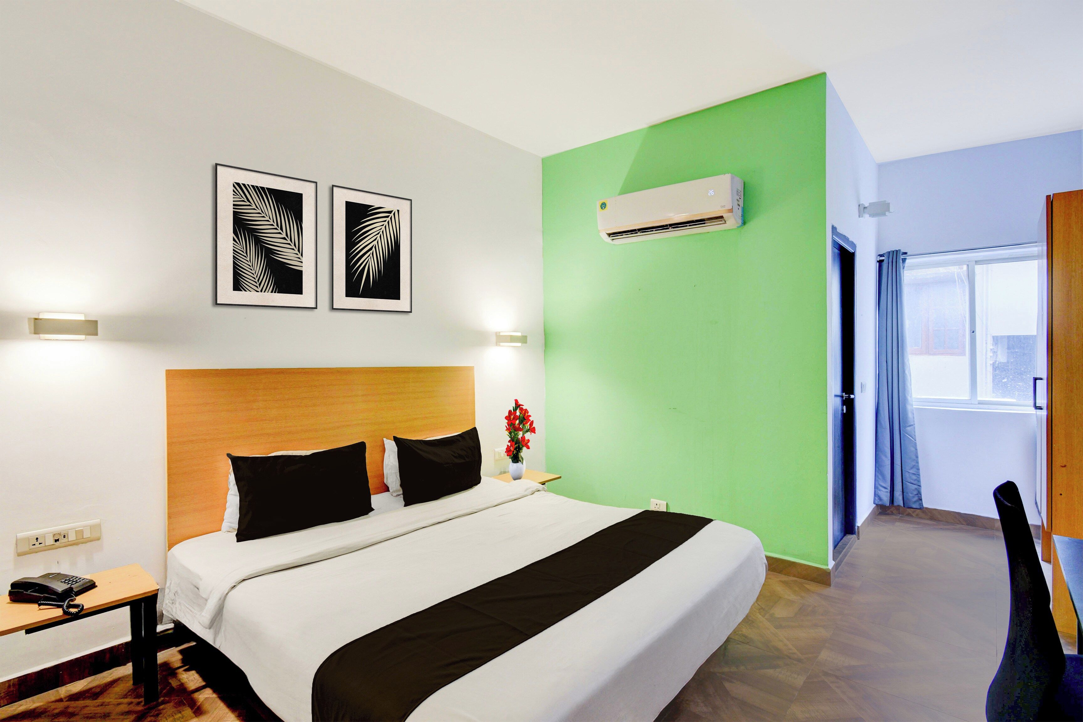 Habitación de hotel con cama, mesita de noche, lámpara, decoración en la pared, unidad de aire acondicionado y vistas al exterior.