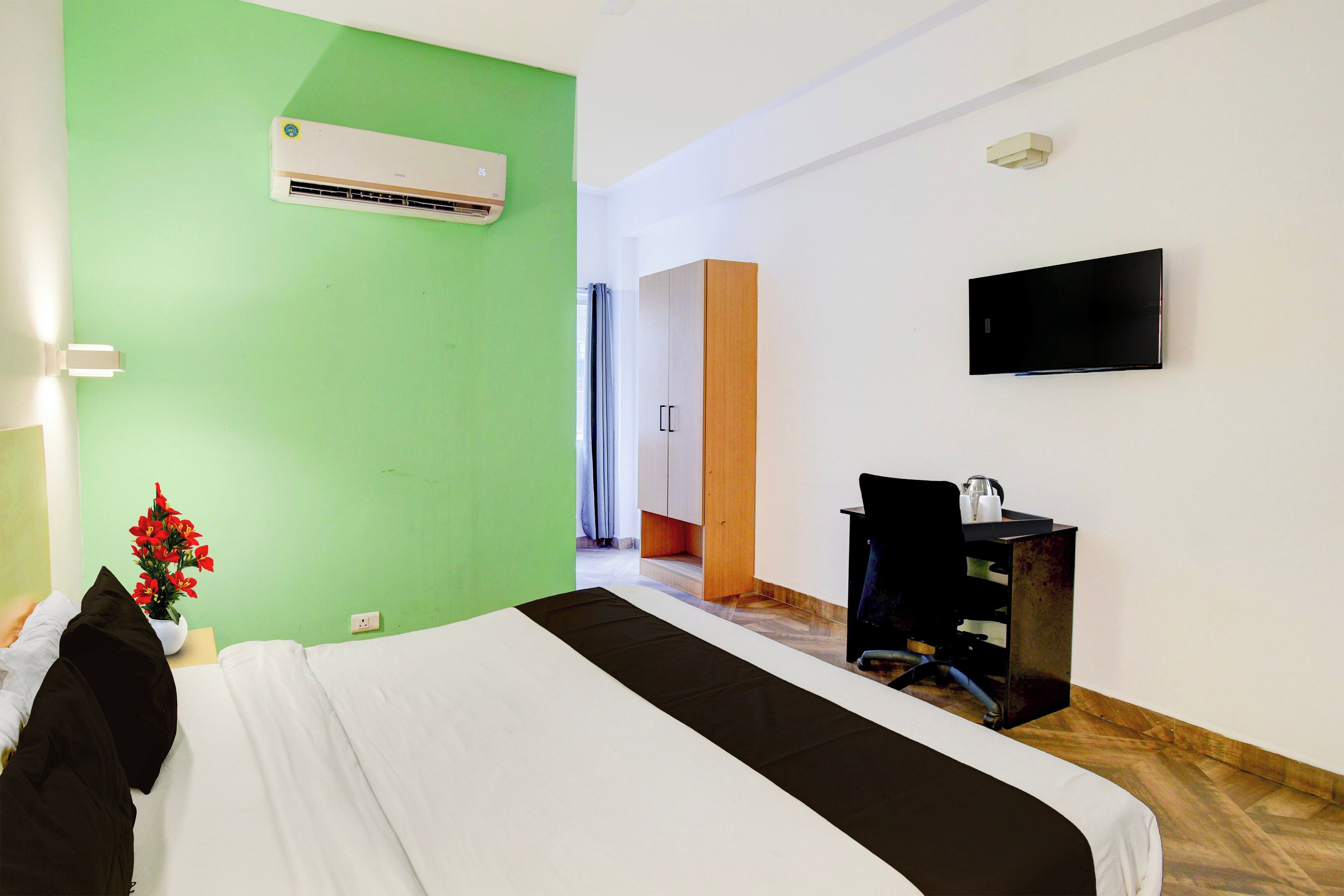 A hotel room with a bed, a desk, a chair, a TV, and an air conditioner.