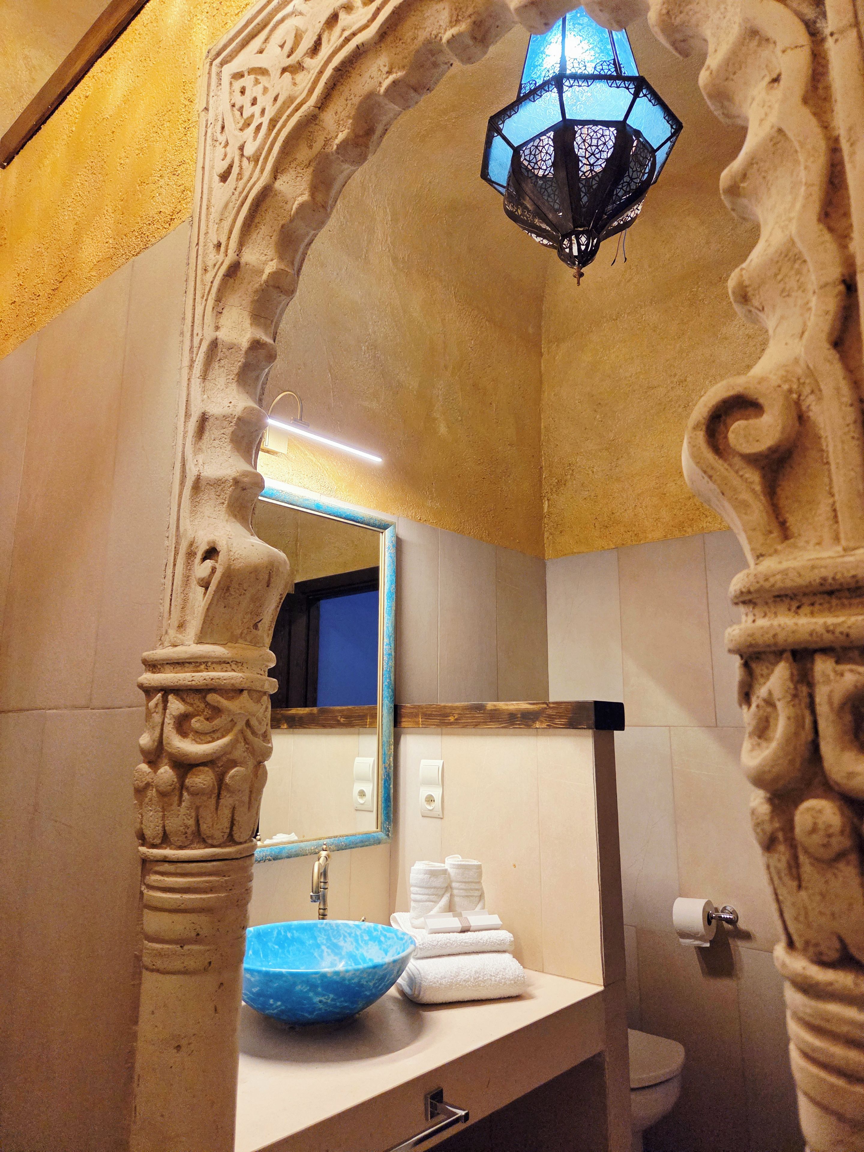 Un baño con un lavabo azul, un espejo y un arco decorativo.