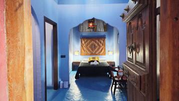 Una habitación con cama, mesita de noche, lámpara y un tapiz colgado en la pared.