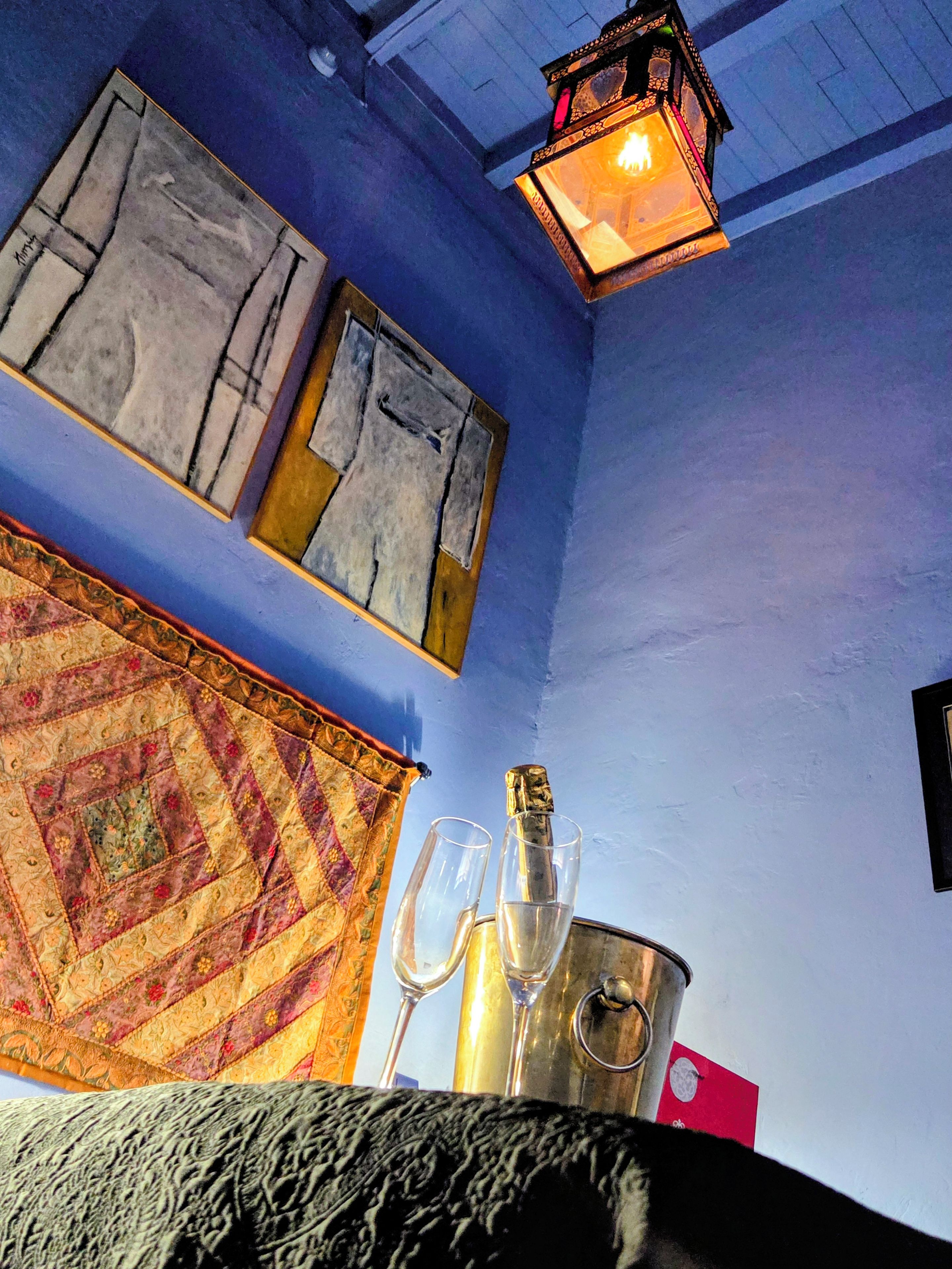 Una habitación con una pared azul, un tapete estampado, un cubo de metal y dos vasos vacíos.