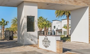 Une entrée moderne de villa avec une façade blanche, des palmiers et un espace clos par un portail.